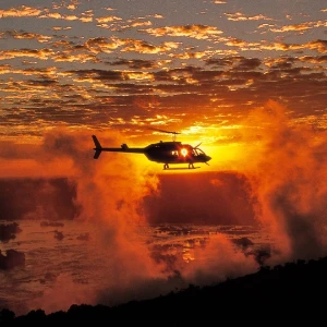 Helicopter silhouetted above Victoria Falls at sunset