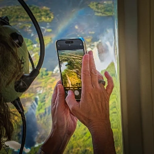 Passenger photographing Victoria Falls from a helicopter with a rainbow below